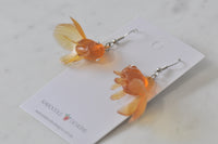 Close-up of goldfish earrings laid on card showing scale texture and tail fins