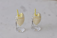 Front view of two banana milkshake drop earrings standing upright showing straw and banana slice detail