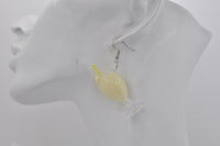 Close-up of a single banana milkshake earring worn on ear, showing glass shape and creamy yellow fill