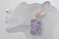 Close-up of single paisley drop earring worn on ear, showing purple and mint pattern