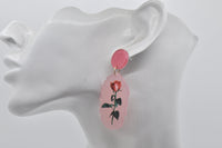 Rose earring shown on ear, close-up of frosted pink drop and glittery pink stud