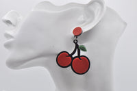 Close-up of red cherry drop earring worn on ear, showing layered Perspex design