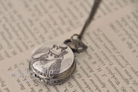 Pocket watch necklace pendant lying open showing Alice illustration and chain