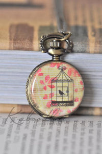 Bronze pocket watch necklace with a birdcage and bird design on an autumn leaf background
