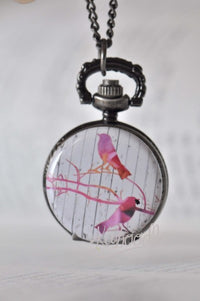 Bird art pocket watch necklace showing two watercolour birds on branches against a wood-look background