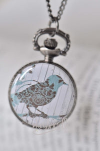 Close-up of pocket watch necklace pendant with a blue bird design on whitewashed panelling