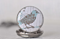 Detail of pocket watch necklace pendant lid featuring a damask patterned blue bird