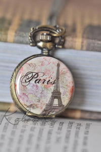 Paris pocket watch necklace pendant with Eiffel Tower and floral design, resting on a book