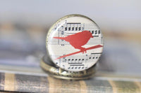 Close-up of red bird pocket watch pendant with musical notation background