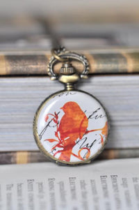 Close-up of orange bird pocket watch pendant with vintage script design and brass filigree bail