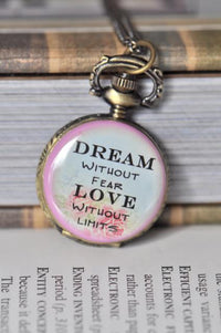 Bronze-tone pocket watch necklace open to show 'Dream Without Fear, Love Without Limits' quote face