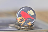 Close-up of red bird and floral pocket watch pendant artwork on antique brass case