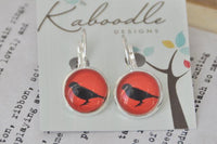 Round clip dangle earrings with black bird silhouette on red background, displayed on Kaboodle card