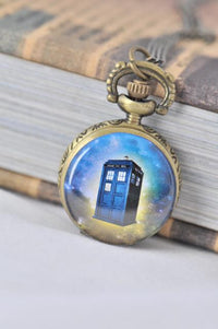 Small brass pocket watch necklace with a blue police box design against a galaxy background