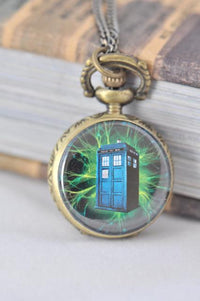 Brass pocket watch necklace with a glowing blue police box design against green sparks