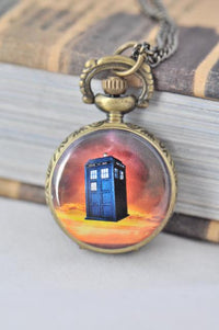 Antique bronze pocket watch necklace with a blue police box design against an orange sky