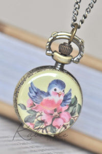 Bronze pocket watch necklace with bluebird and pink blossom design on yellow background
