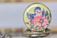 Close-up of bluebird and pink flower design on pocket watch pendant