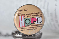 Close-up of hope pocket watch pendant with pink and green cut-out letters on dictionary background