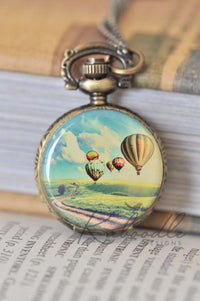 Hot air balloon pocket watch necklace pendant resting on vintage books