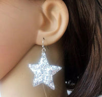 Close-up of silver glitter star earring worn on ear, showing sparkle detail