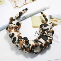 Leopard-print ruffled fabric headband shown flat on a magazine background