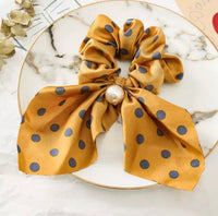 Mustard yellow polkadot scarf scrunchie with faux pearl, laid flat on a marble plate