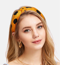 Model wearing a mustard knotted headband with black polka dot print, front view