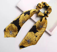 Yellow and black floral satin scrunchie with long scarf-style tails, flat lay view