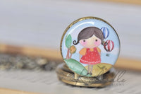 Close-up of pocket watch pendant art featuring girl and hot air balloons