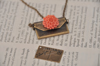 Envelope necklace laid open beside its postcard insert on a book page