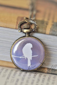 Close-up of a bird silhouette pocket watch necklace resting on stacked books