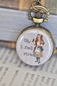 Pocket watch necklace closed, resting on an open book, showing Alice design