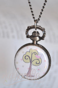 Pocket watch necklace with swirly tree and pink bird design on bronze case, hanging open book background