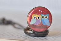 Close up of owl couple pocket watch pendant resting on open book