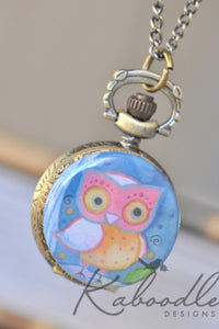 Close-up of pocket watch necklace with a painted pink and blue owl design on the cover