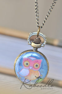 Pocket watch necklace with owl design hanging open on a chain