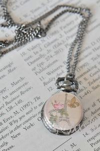 Paris Fleur De Lis pocket watch necklace resting closed on a book page