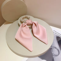 Pink fabric bow scrunchie with faux pearl cluster laid on round display stands