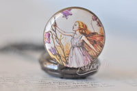 Close-up of purple fairy illustration on pocket watch pendant with orange wings and bellflowers