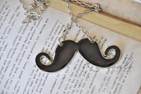 Close-up of glossy black moustache pendant resting on an open book page