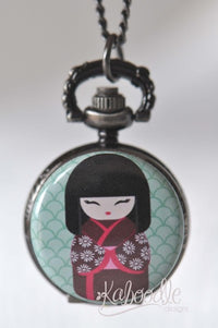 Kokeshi doll pocket watch necklace with floral kimono design on mint background