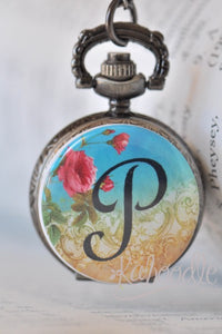 Rose and initial P pocket watch necklace closed, showing pink rose design on blue and gold background