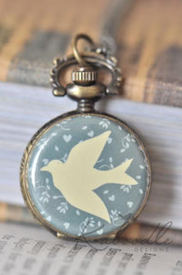 Close-up of bird silhouette pocket watch pendant with dusty blue floral background and heart details